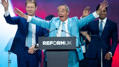 Nigel Farage at a Reform UK podium, arms outstretched, with two men in suits beside him on stage.