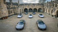 Multiple Polestar 5 electric cars parked in a stone courtyard of Alnwick Castle, under a cloudy sky.