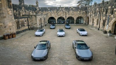 Multiple Polestar 5 electric cars parked in a stone courtyard of Alnwick Castle, under a cloudy sky.