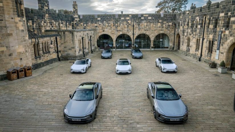 Multiple Polestar 5 electric cars parked in a stone courtyard of Alnwick Castle, under a cloudy sky.