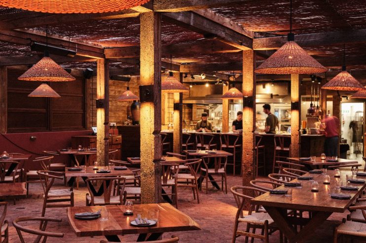 Inviting interior of Pyro restaurant with rustic wooden tables, woven pendant lights, and visible kitchen staff.