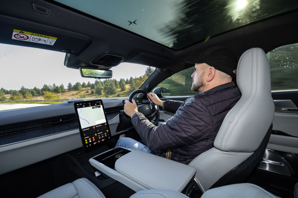 Man driving a modern car with a large central display showing navigation, sunny weather.