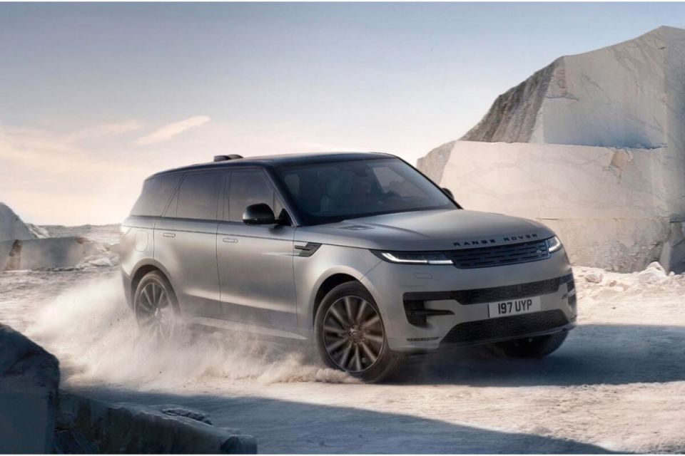 Silver Range Rover Sport driving on a dirt road, kicking up dust, with large white rock formations in the background.