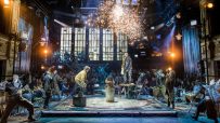 Energetic Rent musical review with performers on stage, a guitarist on a table, and sparks flying.