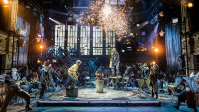 Energetic Rent musical review with performers on stage, a guitarist on a table, and sparks flying.