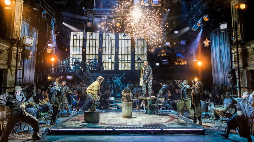 Energetic Rent musical review with performers on stage, a guitarist on a table, and sparks flying.