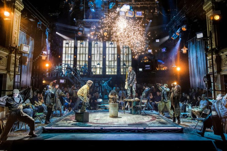 Energetic Rent musical review with performers on stage, a guitarist on a table, and sparks flying.
