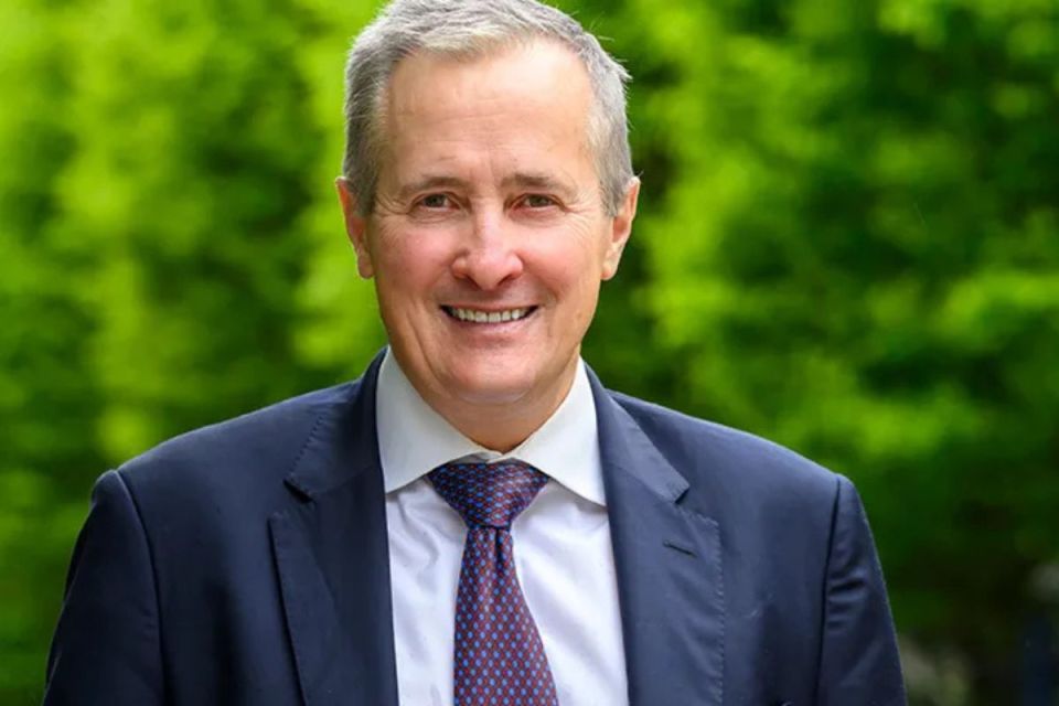 Rob Perrins, CEO of Berkeley Group, smiling in a navy suit and patterned tie outdoors with green foliage
