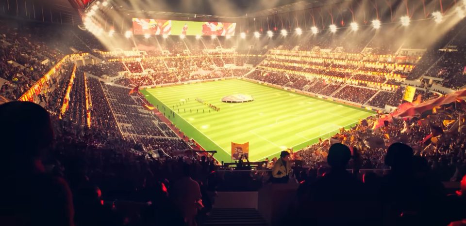 Large, packed football stadium at night with bright lights, a green field, and cheering fans in the stands.