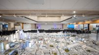 Detailed architectural model of a city, with empty chairs arranged for a presentation in the background.