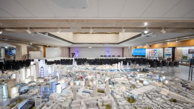 Detailed architectural model of a city, with empty chairs arranged for a presentation in the background.