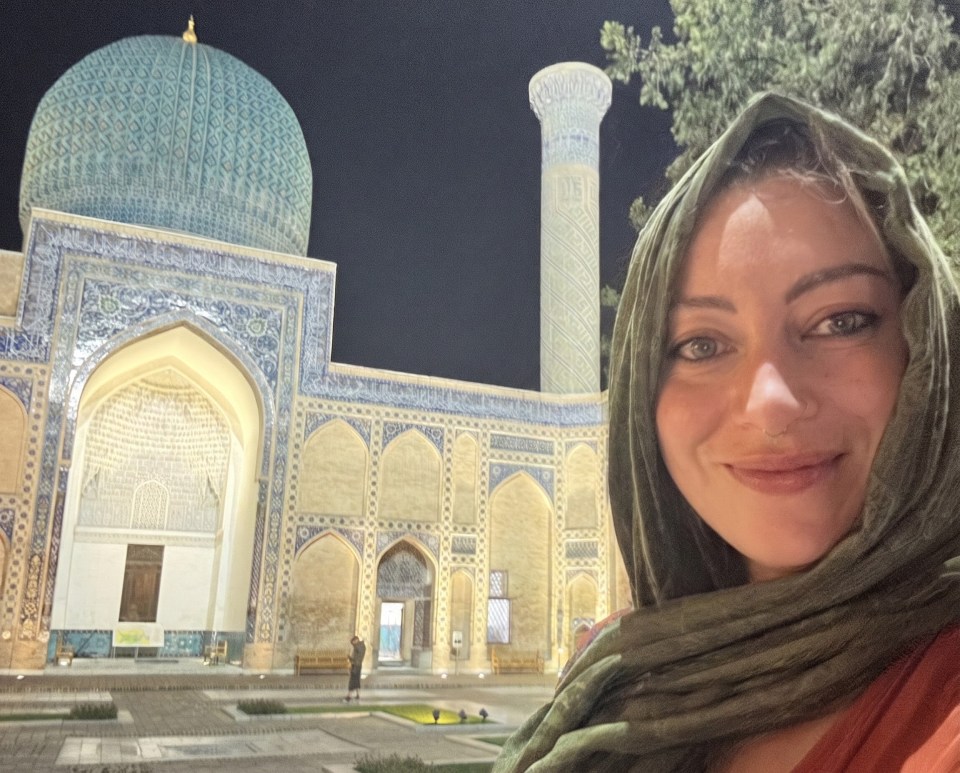 Woman in green headscarf smiling, with a blue-domed mosque and minaret lit at night in the background