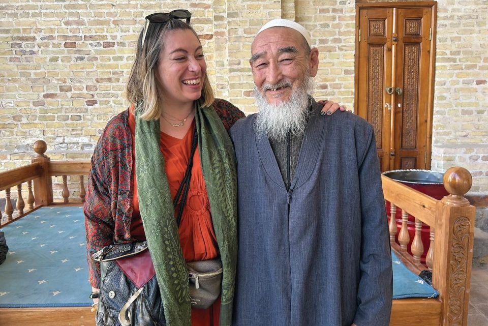 Smiling woman and elderly man with white beard, possibly on the Silk Road, in traditional setting.