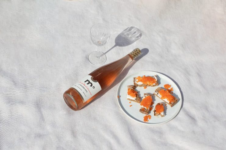 Sober October rosé wine bottle next to a wine glass and crackers with cream cheese and caviar on a white cloth