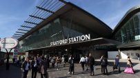 Stratford Station exterior with modern glass architecture and pedestrians on a sunny day