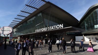 Stratford Station exterior with modern glass architecture and pedestrians on a sunny day
