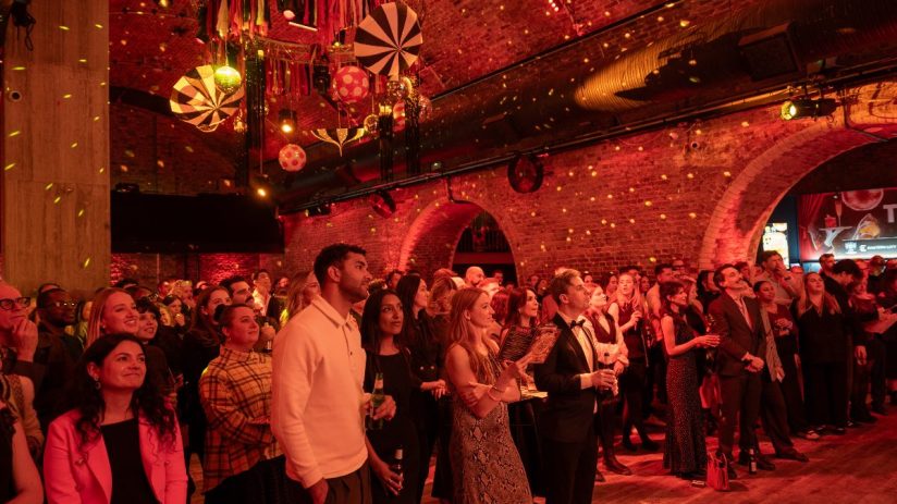 Attendees at the Toast the City Awards event, looking towards a stage under red lighting and brick arches.