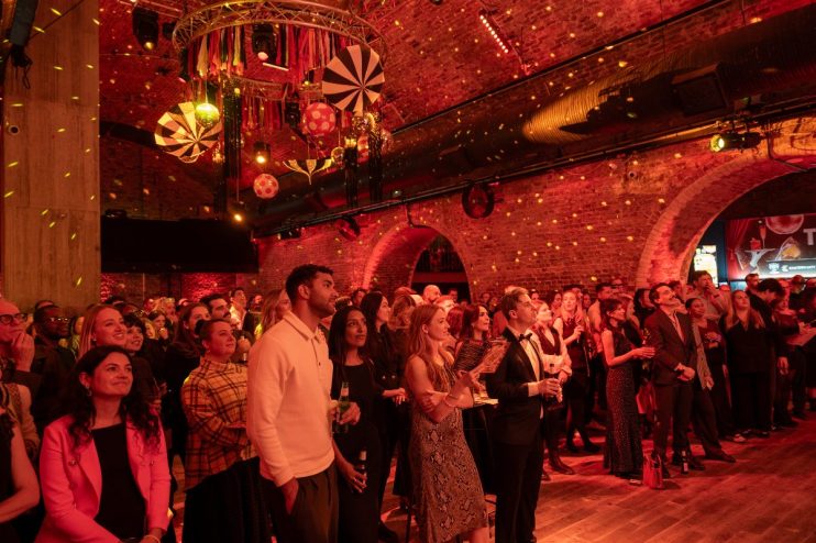 Attendees at the Toast the City Awards event, looking towards a stage under red lighting and brick arches.