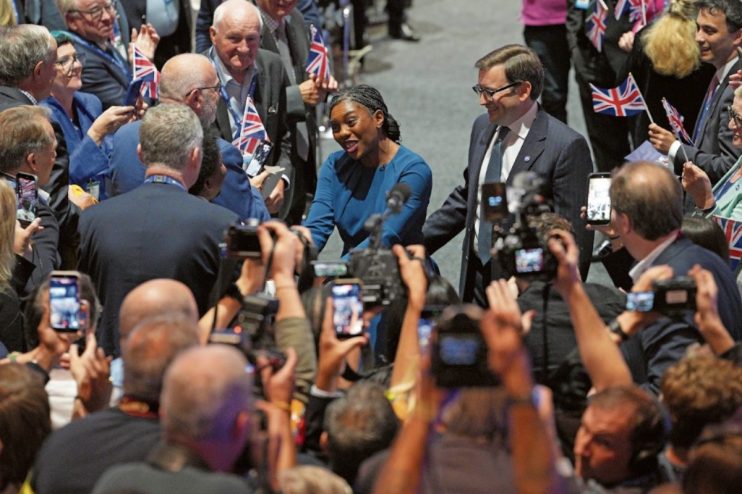 Kemi Badenoch and Kwasi Kwarteng smiling, surrounded by a crowd holding up phones and Union Jack flags at the Tory confere...
