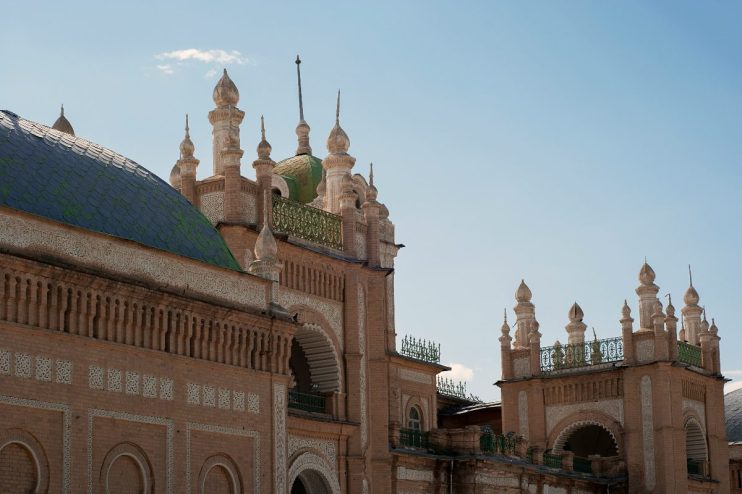 Ornate Uzbek architecture with a tiled dome and decorative brickwork under a clear sky, Silk Road travel.