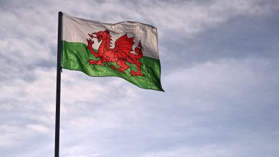 Welsh flag, Y Ddraig Goch, with a red dragon against white and green stripes, flying against a cloudy sky.