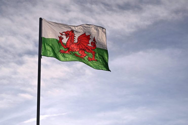 Welsh flag, Y Ddraig Goch, with a red dragon against white and green stripes, flying against a cloudy sky.