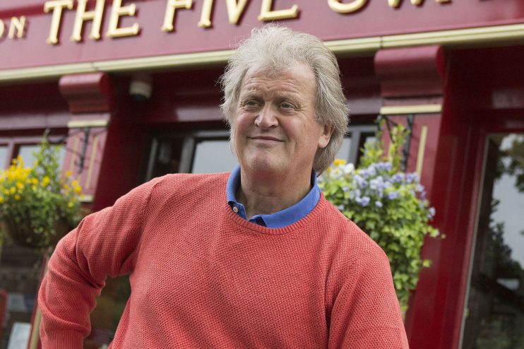 Wetherspoon chairman Tim Martin smiling in a red sweater outside a pub with hanging baskets