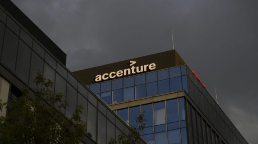 Accenture office building facade with logo visible against a dark, cloudy sky.