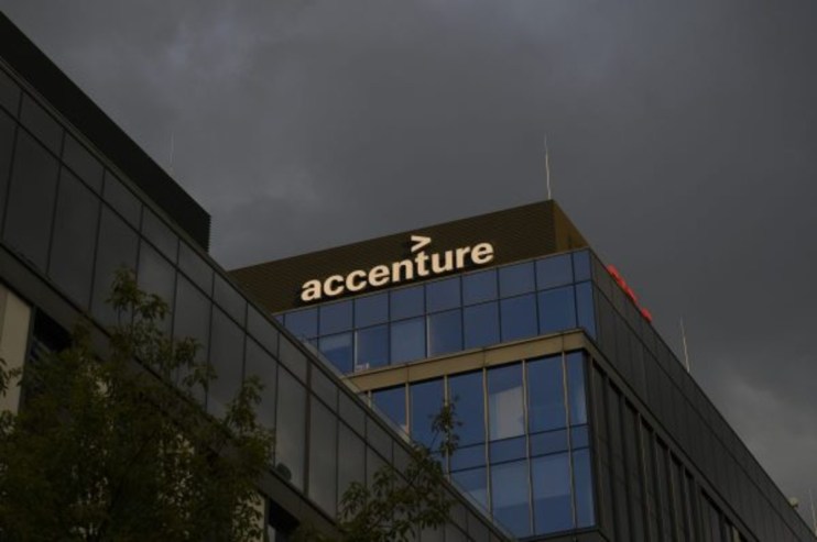Accenture office building facade with logo visible against a dark, cloudy sky.
