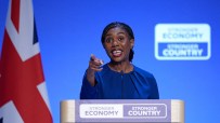 Kemi Badenoch, a politician, speaks at a podium with a Union Jack flag and Stronger Economy, Stronger Country signs.