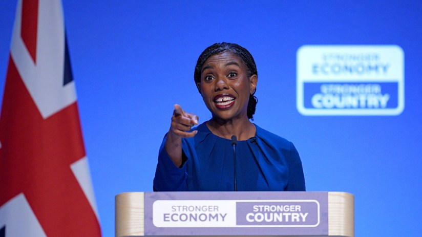 Kemi Badenoch, a politician, speaks at a podium with a Union Jack flag and Stronger Economy, Stronger Country signs.