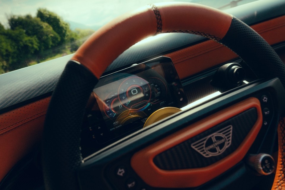 Donkervoort steering wheel and digital dashboard with orange accents and a view of trees