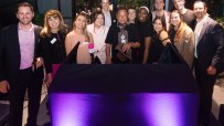 Group of diverse professionals gathered behind a table with purple uplighting, celebrating an Eastern City BID proposal.