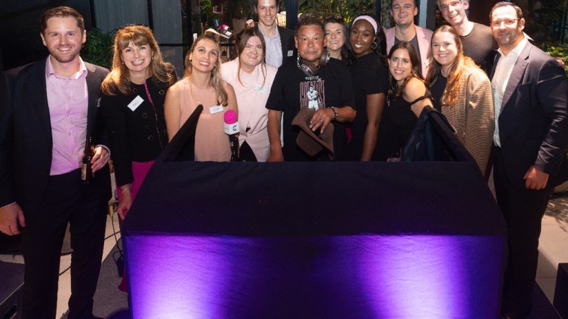 Group of diverse professionals gathered behind a table with purple uplighting, celebrating an Eastern City BID proposal.