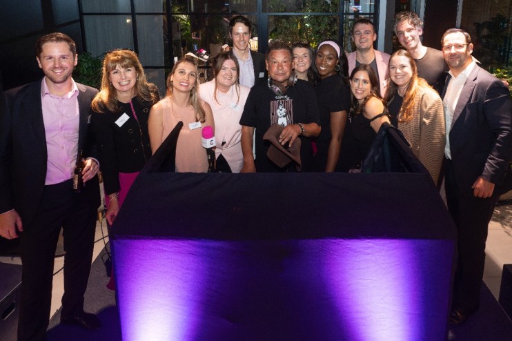 Group of diverse professionals gathered behind a table with purple uplighting, celebrating an Eastern City BID proposal.