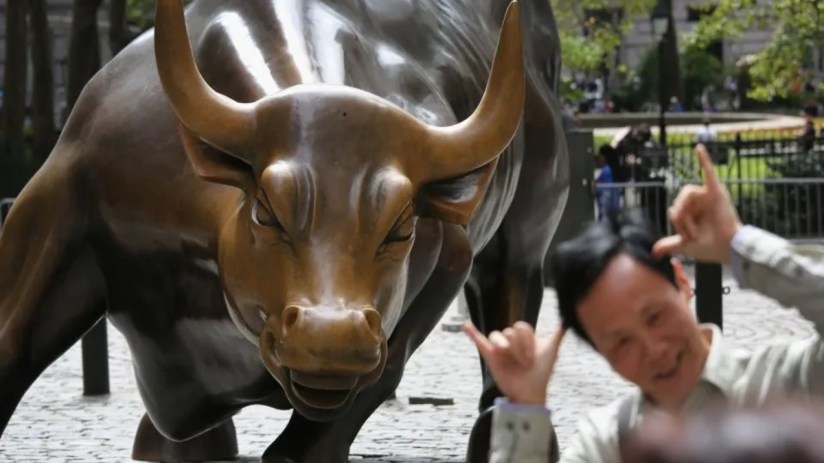 Wall Street Charging Bull statue with a man smiling and making shaka gestures in front of it