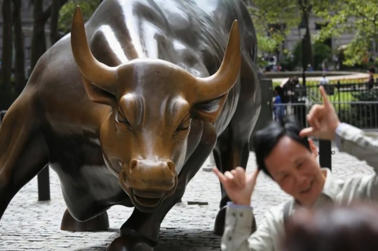 Wall Street Charging Bull statue with a man smiling and making shaka gestures in front of it