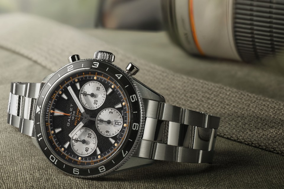 Gallet 1826 Multichron Pilot watch with black dial, white sub-dials, and steel bracelet, on a textured surface