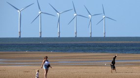 Offshore wind farm turbines visible from a sandy beach with people enjoying the shore.