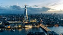 Aerial view of London cityscape at dusk, featuring The Shard, River Thames, and illuminated bridges and buildings
