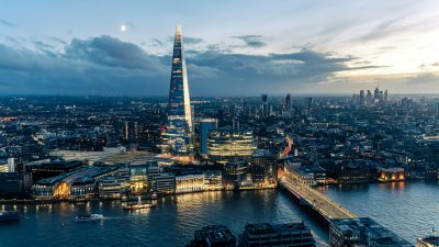 Aerial view of London cityscape at dusk, featuring The Shard, River Thames, and illuminated bridges and buildings