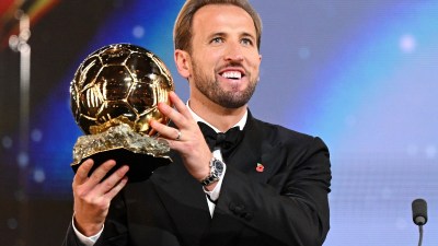 Harry Kane in a tuxedo, holding a golden football trophy, wearing a Rolex Daytona watch.
