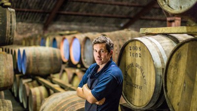Man in a blue shirt and apron standing among whisky barrels at Glengoyne Distillery, Dumgoyne.