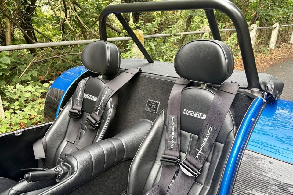 Interior of a blue Caterham Seven 310 sports car with black leather seats and Encore-branded harnesses