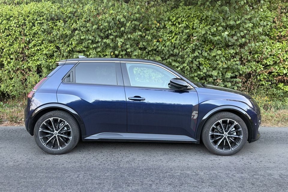 Dark blue compact car parked on asphalt, side view, with a green hedge in the background.