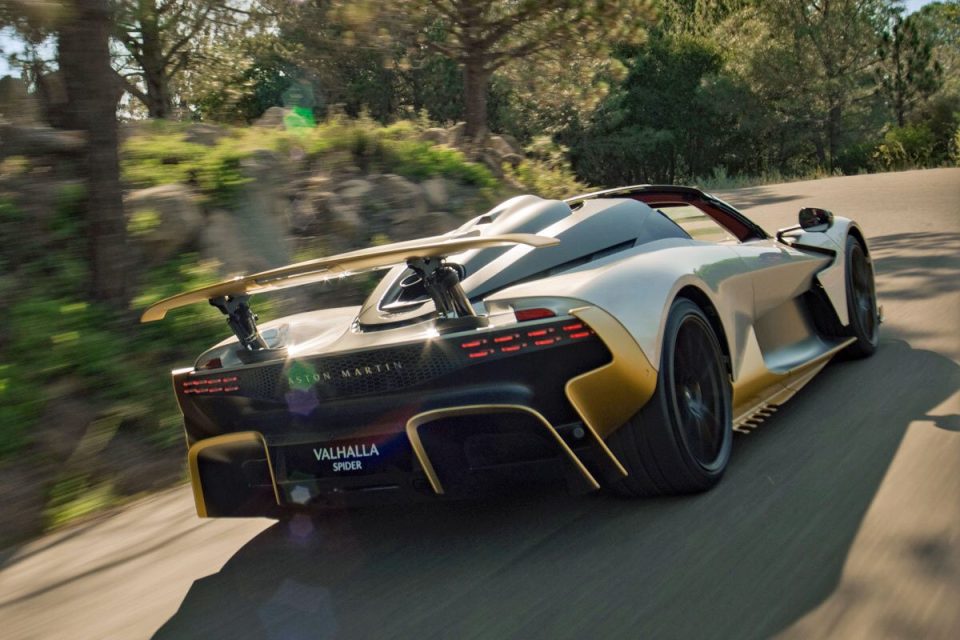 Rear view of the silver and gold Aston Martin Valhalla Spider sports car on a winding road.