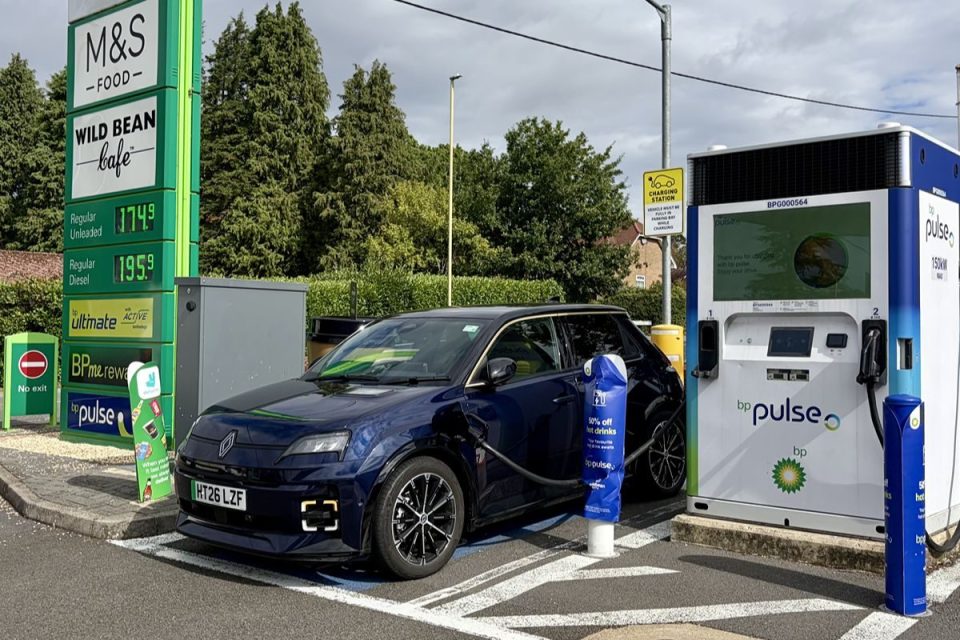 Dark blue electric car charging at a BP Pulse station with M&S Food and fuel prices in the background.