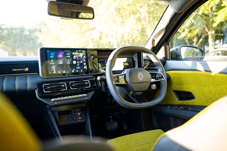 Renault 5 interior showing dashboard, steering wheel, infotainment screen, and lime green fabric accents.