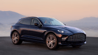 Dark blue Aston Martin DBX luxury SUV parked outdoors with mountains in the background at sunset.