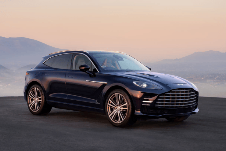 Dark blue Aston Martin DBX luxury SUV parked outdoors with mountains in the background at sunset.